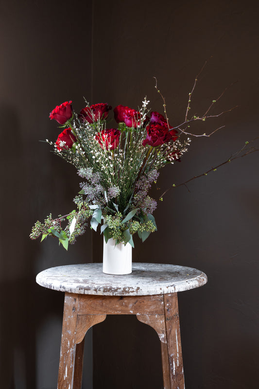 A classic and romantic flower arrangement featuring one dozen (12) long stem, red roses and lush greenery designed in a tall modern ceramic vase 