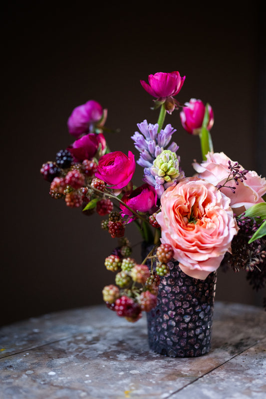 A detailed view of the Love You Berry Much Arrangement coral garden roses, fuchsia ranunculus, lavender hyacinth, hot pink tulips and black berry